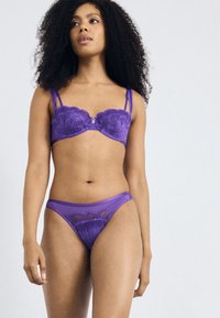 Purple lingerie set featuring a lace balconette bra with floral patterns and adjustable straps, paired with matching high-cut thong.
