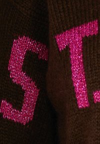 Tessuto lavorato a maglia marrone con la scritta luccicante di un brillante colore rosa "S.T." ben in evidenza. La consistenza sembra morbida e calda.