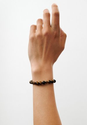 Hand raised against white background, wearing a round brown and black beaded bracelet on the wrist.