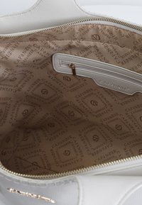 Witte leren handtasinterieur met een tan voering, voorzien van een herhaald logo patroon. Inclusief een ritsvak aan de ene kant en gouden hardware.