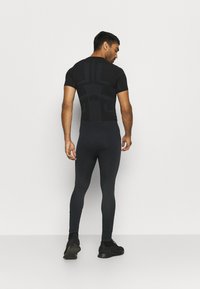 Top deportivo negro de manga corta con diseño texturizado, combinado con leggings negros ajustados que tienen un patrón en la parte inferior de la pierna, llevados con zapatos negros.