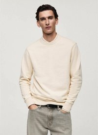 Cream-colored sweatshirt with a round neck, ribbed cuffs, and hem. Worn with light grey jeans. Smooth texture, minimal design.