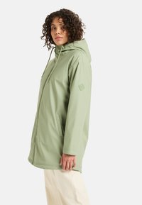 Svetlozelená vodoodolná bunda s kapucňou, sťahovacou šnúrkou a bočnými vreckami. Hladká textúra s emblémom na ľavom rukáve.