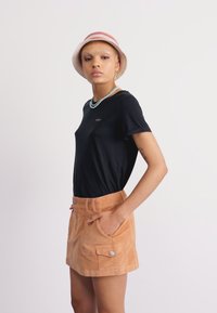 Zwarte t-shirt met korte mouwen met een kleine print, gecombineerd met een lichtoranje leren mini-rok met zijzakken en zilveren hardwareaccenten.