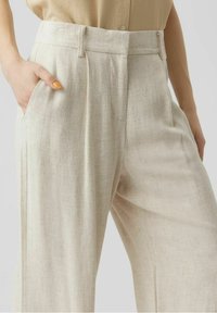 Beżowe lniane spodnie o luźnym kroju, z plisami z przodu, kieszeniami po bokach i gładką fakturą. Lekki i oddychający materiał.