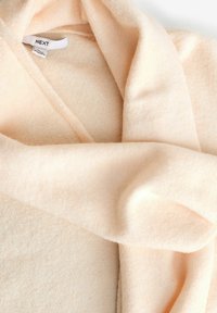 Světle broskvový měkký pletený svetr vyrobený z vlněné směsi, s uvolněným střihem a hlubokým výstřihem do V. Štítky viditelné uvnitř límce.
