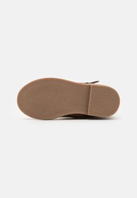 Semelle de chaussure marron montrant une surface en caoutchouc texturée avec une finition à motif, un design plat et un léger talon à l'arrière.