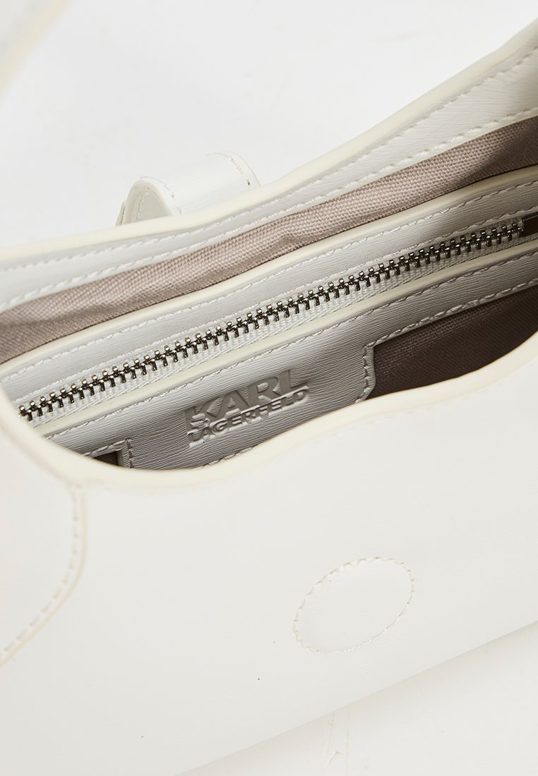 Sac à main structuré blanc avec un extérieur en cuir lisse, doublure en tissu beige, poche zippée intérieure et détail de logo en relief à l'intérieur.