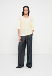 Világos sárga, puha anyagú felső háromnegyedes ujjakkal, laza, sötétkék, széles szárú farmerrel és fekete, hegyes orrú cipővel párosítva.