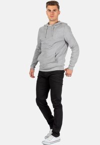 Sweatshirt à capuche gris avec une poche kangourou, associé à un jean noir et des baskets blanches. Look décontracté avec un cordon de serrage à la capuche.