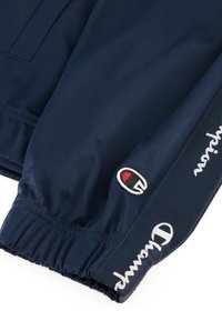 Navy blue windbreaker with elastic cuffs, featuring embroidered Champion logo and white text along the sleeve, made from smooth synthetic material.