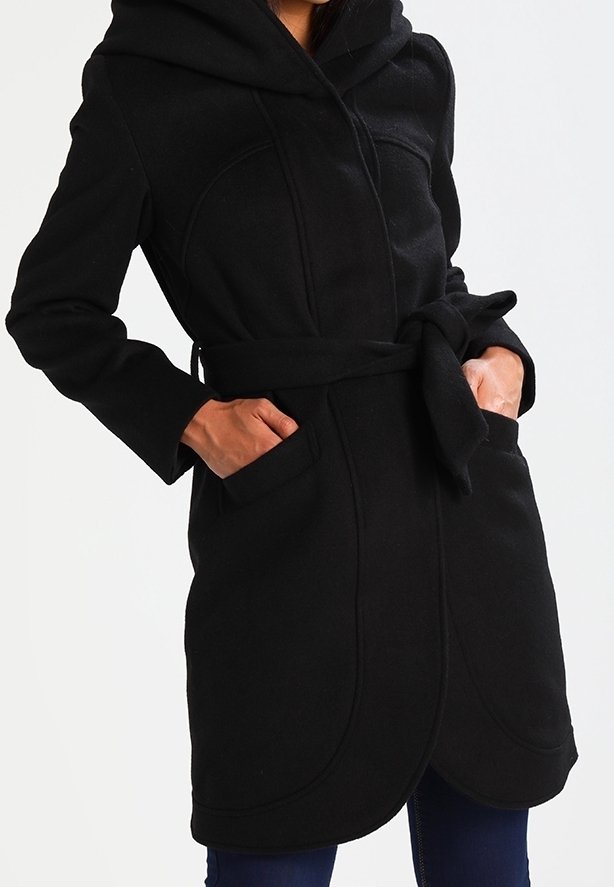 Svart huva jacka i mjukt tyg, med bälte i midjan, sidofickor och rundad fåll med sömdetaljer.