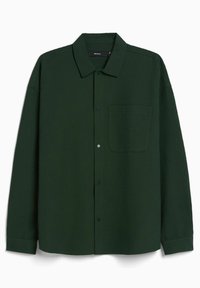 Zelená košile na knoflíky z texturované látky. Má límec, přední kapsu, dlouhé rukávy a zaoblený spodní lem.