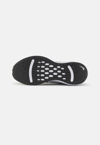 Sole di scarpa da corsa Nike in bianco e nero con motivo testurizzato per la presa e logo swoosh Nike sul bordo del tallone su sfondo bianco uniforme.
