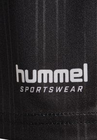 Svart sportklädesmaterial med en strukturerad yta, som har en vit "hummel"-logotyp och texten "SPORTSWEAR". Vertikal randig mönster synligt.