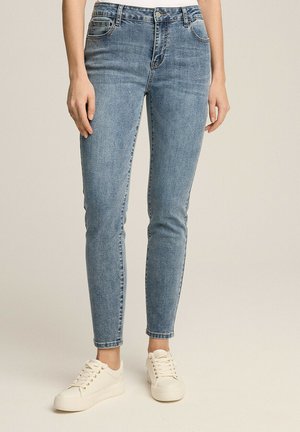 Niebieskie rurki z denimu, charakteryzujące się klasycznym pięciopocketowym designem, kontrastowym przeszyciem i średnim stanem, zestawione z białymi sneakersami.