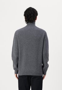 Grau gerippter Rollkragenpullover aus einem strukturierten Strickmaterial, mit einem schmalen Kragen und weiten Ärmeln, sichtbaren Nähdetails und einer lässigen Passform.