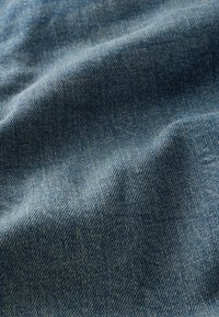 Niebieska tkanina dżinsowa z widocznym ukośnym wzorem tkania oraz delikatnymi fałdami tworzącymi subtelne cienie i fakturę.