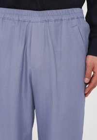 Helle blaue Hose mit einem elastischen Bund, Falten und seitlichen Taschen. Glatte Textur und maßgeschneiderter Schnitt, geeignet für lässige Kleidung.