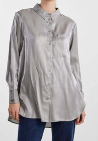 Camicia a maniche lunghe con bottoni in satin grigio chiaro, con colletto, taschino sul petto e orlo leggermente arrotondato. Presenta maniche con polsini.