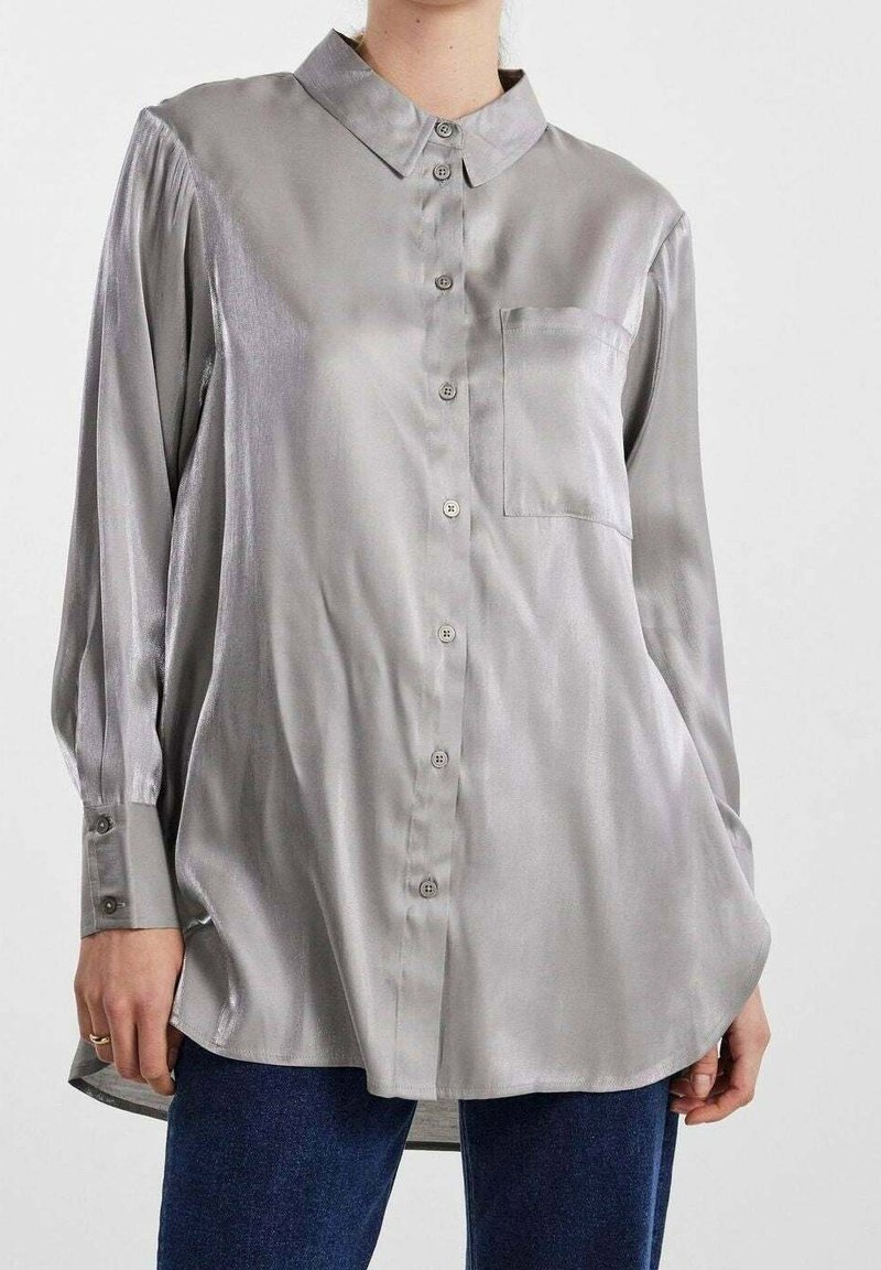 Camisa de manga larga abotonada en satén gris claro con cuello, un bolsillo en el pecho y dobladillo ligeramente redondeado. Presenta mangas con puños.