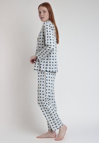 Conjunto de pijama coordinado en gris claro con patrones de corazones en azul marino. La parte superior tiene mangas largas y un cuello redondo; los pantalones son de corte recto.