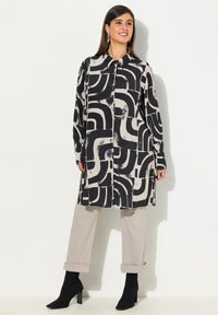 Langarmshirt met abstract zwart en crèmekleurig patroon, knoopsluiting aan de voorkant en een iets losse pasvorm. Gecombineerd met lichtbeige broek met opgerolde mouwen.