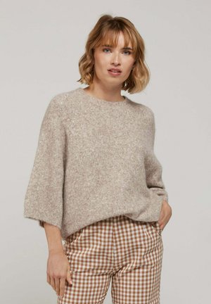 Pull en laine beige clair avec une coupe ample, col rond et manches trois-quarts, associé à un pantalon à carreaux vichy marron et blanc.