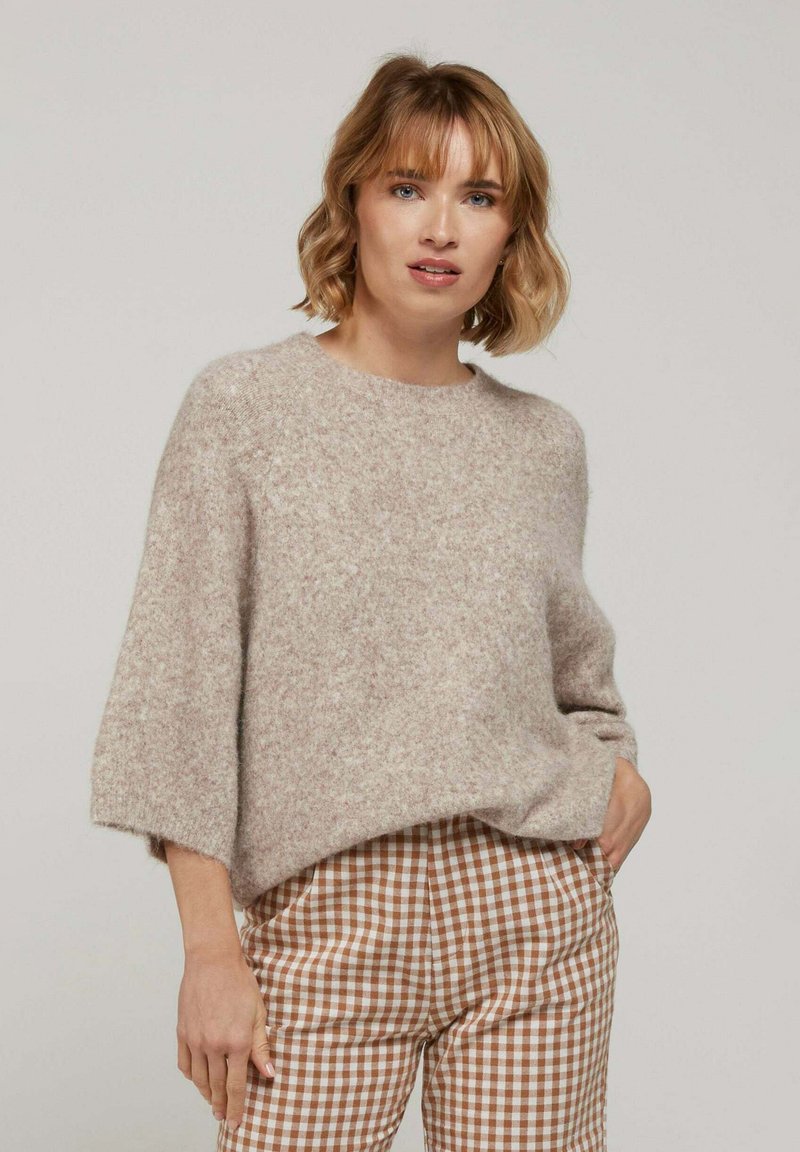 Pull en laine beige clair avec une coupe ample, col rond et manches trois-quarts, associé à un pantalon à carreaux vichy marron et blanc.