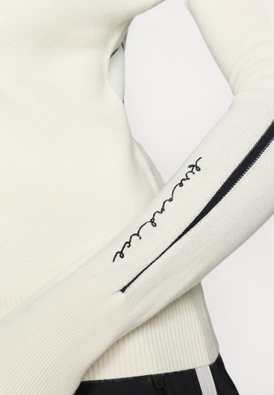 Πλεκτό λευκό πουλόβερ με ραβδωτή υφή, που διαθέτει μαύρη λωρίδα στο πλάι και κεντημένα στοιχεία στα μανίκια.