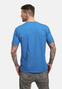 Camiseta azul de manga corta en tejido suave, con cuello redondo, textura lisa y costuras mínimas, combinada con jeans grises.