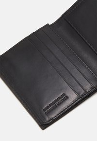 Black leather wallet interior with multiple card slots, subtle texture, and embossed “Genuine Leather” detail. Stitched edges.