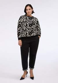 Maglione a motivo floreale in bianco e nero con scollo rotondo, abbinato a pantaloni neri con dettagli decorativi e risvolti arrotolati.