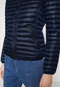 Giubbotto imbottito navy con texture trapuntata, zip frontale e due tasche laterali con zip. Le maniche hanno polsini elastici. Il materiale è liscio.