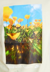 Tricou din bumbac cu un grafic vibrant de flori galbene pe un fundal de cer albastru, cu textul "Îndreaptă-te spre natură." și logo-ul Nike în alb.