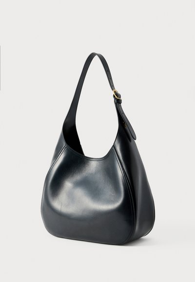 Mustast siledast nahast õlakott, reguleeritava sangaga ja kuldse pandlaga, kumer siluett ning minimaalsed õmblused.