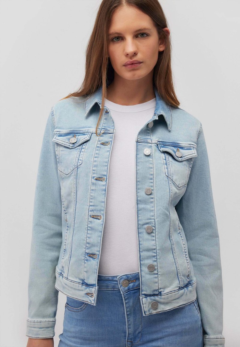 Giacca di jeans azzurro chiaro con un design classico. Presenta tasche sul petto, chiusura con bottoni e una texture leggermente invecchiata.