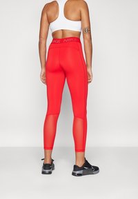Rode sportleggings met een hoge tailleband, voorzien van meshpanelen en een gladde textuur. Draag ze met een witte sportbeha en zwarte sneakers.