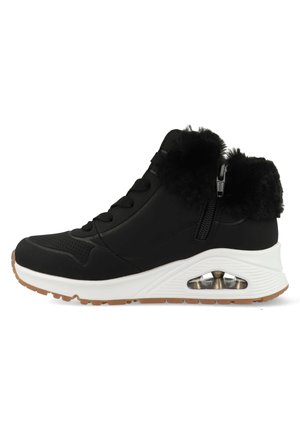 Zapatillas deportivas negras con una parte superior texturizada, cuello de pelo sintético, detalle de cremallera y una mediasuela blanca con un comprimido de aire visible en el talón.