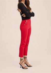 Un pantalon rouge taille haute fuselé avec des accents de boutons à l'avant et des poches. Associé à un haut noir ajusté à manches longues et des talons noirs avec des lanières.