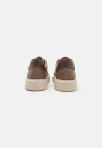 Braune Ledersneaker mit glatter Oberfläche, ausgestattet mit einer kontrastierenden dunkelbraunen Ferse und einer beigefarbenen Gummisohle, die ein minimalistisches Design zeigen.