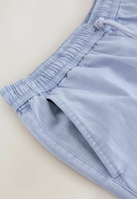 Shorts en tissu bleu clair avec taille élastique, poche latérale et détail de cordon, sur un fond neutre.