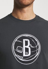 T-shirt en coton gris avec un grand motif blanc représentant un ballon de basket avec un "B" majuscule à l'intérieur, de forme ronde, à manches courtes et col rond.