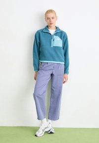 Light blue fleece pullover with a half-zip collar and a chest pocket. Paired with lavender straight-leg trousers and white and silver sneakers.
