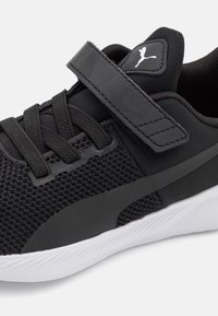 Černá sportovní bota s pleteným textilem, širokým suchým zipem a bílou gumovou podrážkou. Disponuje texturovaným designem s logem.