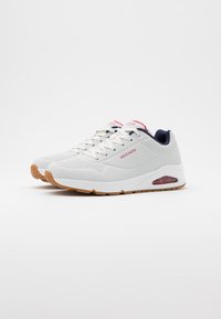 White athletic shoes made of mesh and synthetic materials, featuring a gum rubber sole, padded collar, and a subtle red and navy accent.