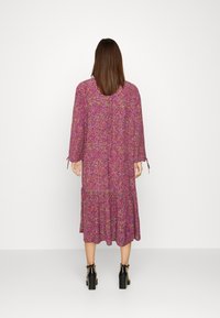 Un lungo abito floreale con un motivo rosa e viola, maniche lunghe con dettagli a fiocco e orlo a balze stratificate.