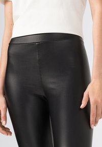 Svarta leggings i konstläder med en slät yta och hög midja, med en figurnära design som framhäver benens form.