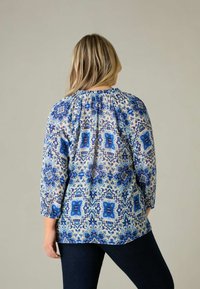 Blusa blu a fantasia con maniche a tre quarti e scollo arricciato. Presenta disegni intricati in diverse tonalità di blu su uno sfondo chiaro.