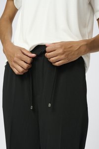 Pantaloni neri con una cintura regolabile, caratterizzati da punte metalliche argento. Abbinati a una maglietta grigia chiara a maniche corte.